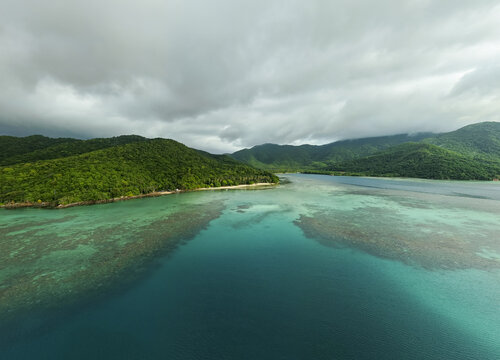 Aerial view of the vibrant turquoise sea meeting the lush green coastline under a dramatic sky, Karimunjawa, Central Java, Indonesia.