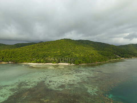 Aerial view of a lush, verdant island meeting the turquoise sea under a brooding sky, Karimunjawa, Central Java, Indonesia.