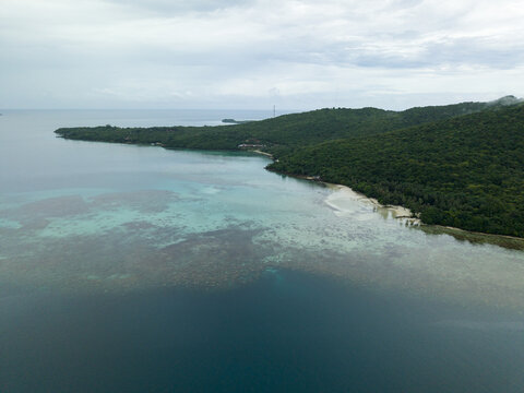 Aerial view of the coastline where the deep blue sea meets the vibrant shallows and lush green land, Karimunjawa, Central Java, Indonesia.