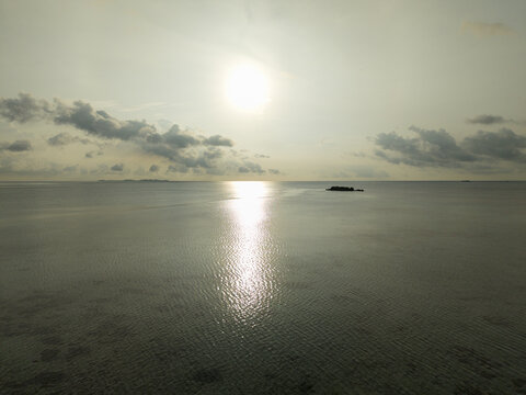 Aerial view of the sun reflecting off the calm sea waters, with a distant island silhouette against the horizon at Bobby Beach, Karimunjawa, Central Java, Indonesia.