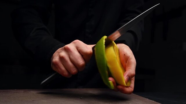 Chef peels mango with knife, showcasing continuous slicing action in kitchen