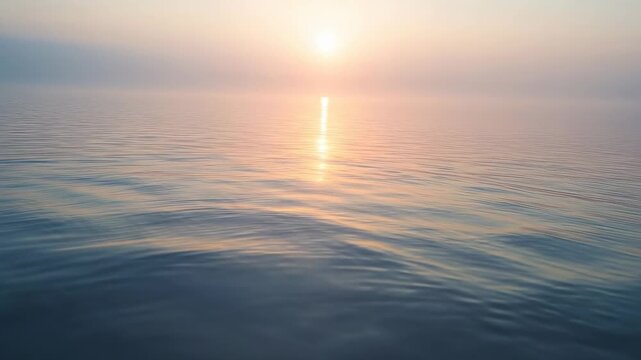 Brightening low sun rising above horizon, causing reflection shifting on calm ocean with ripples