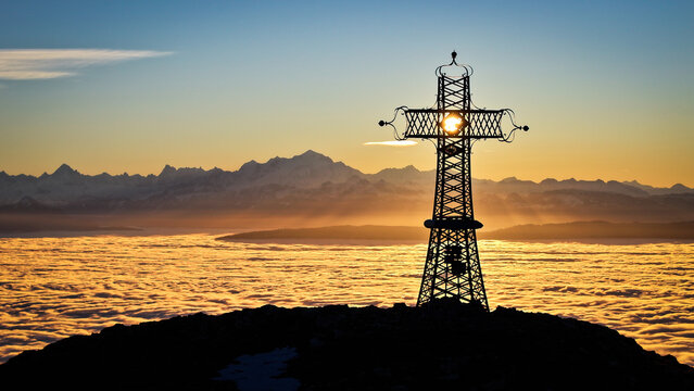 Aerial view of the cross silhouetted against the golden sunset and cloud inversion over the Jura mountains, Le Reculet, Thoiry, Auvergne-Rhone-Alpes, France.