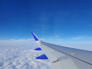 Obraz premium Phone photo of a blue sky over clouds with an airplane wing in view. Aerial travel scene showing altitude, flight perspective, and serene cloudscape.