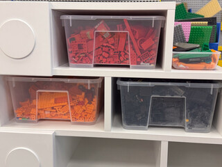 Naklejka premium Clear bins of sorted lego bricks on white cubby shelf