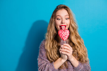 Young woman with heart shaped lollipop smiles against blue background for fashion lifestyle...