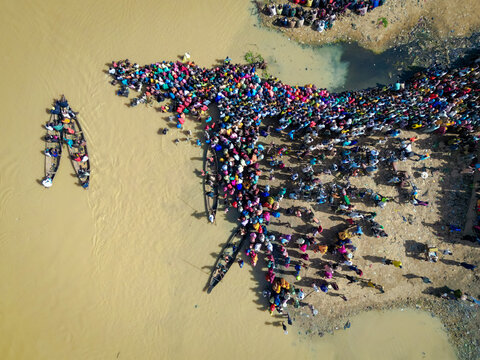Aerial view of a dense gathering of people by the riverbank, with boats ferrying more to the shore, Argungu, Kebbi, Nigeria.