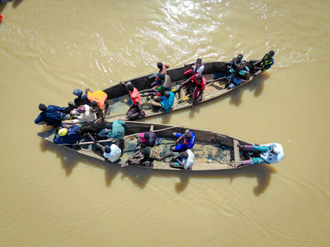Aerial view of people on wooden boats navigating the muddy waters, creating ripples in the vast expanse of the river, Argungu, Kebbi, Nigeria.