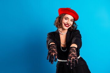 Young chic woman wearing a red beret black outfit with lace gloves smiling against blue background