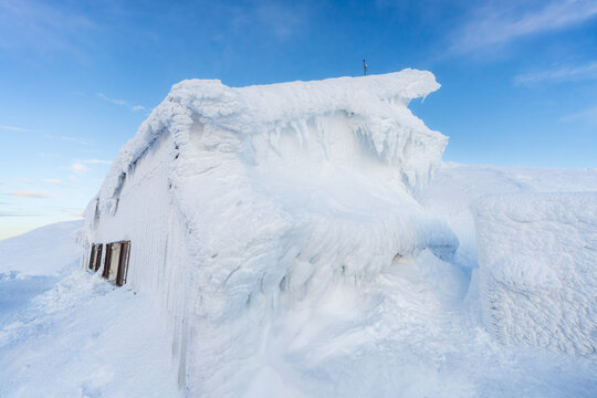 View of a snow-laden building with a thick, frosted layer against a clear sky, creating a serene winter scene, Sneznik, Ilirska Bistrica, Slovenia.