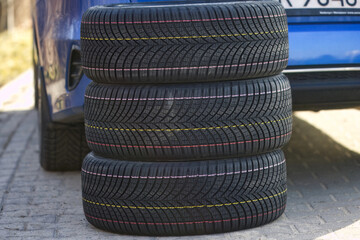 A stack of new all season tires against the background of a passenger car, illustrating tire replacement in autumn or spring and all-season tires as an alternative to seasonal tires. © Robert