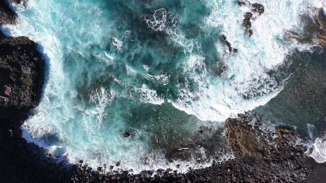 Aerial view of turquoise ocean waves crashing against rocky shoreline. Dynamic movement of water and foam in coastal environment with clear blue hues. Vibrant turquoise water in a coastal setting