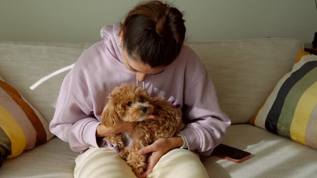 Caring woman lovingly kisses her little dog while seated on cozy sofa