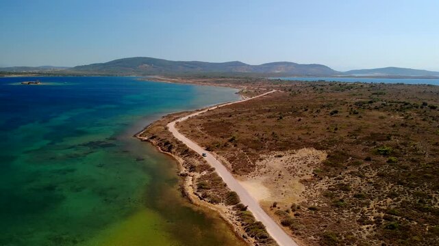 Aerial view of the vivid, turquoise waters meeting the arid coastline with a road winding through the landscape, Cunda Island, Ayvalik, Balikesir, Turkey.