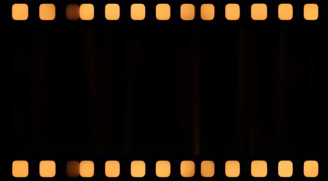 Abstract dark photographic film negative with illuminated sprocket holes in warm colors