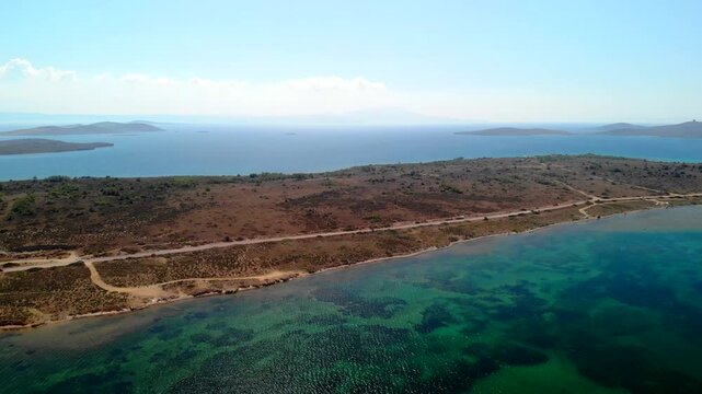 Aerial view of an island with a road cutting through, showing the contrast between the clear blue sea and the arid land, Cunda Island, Ayvalik, Balikesir, Turkey.