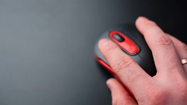 Close-up of a hand moving a black and red wireless mouse on a clean dark desk with copy space, showing office productivity and computer navigation in a minimal workspace.