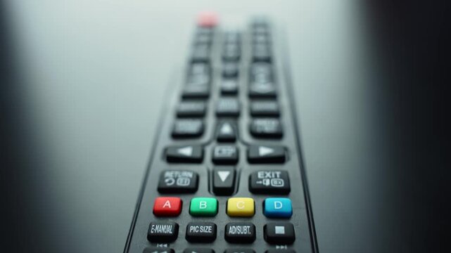 TV remote control lying on a dark surface with shallow depth of field and copy space, showing volume and menu buttons for home entertainment, streaming, and user interface navigation.