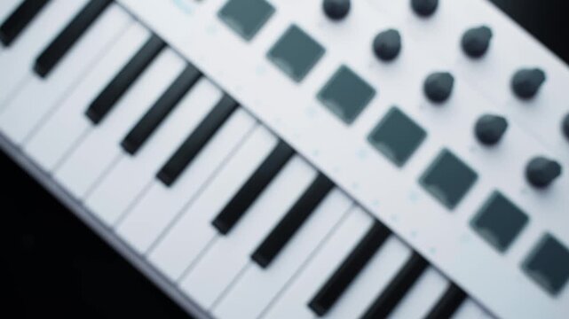 Close-up of a white MIDI keyboard controller with piano keys, pads and knobs on a desk. Shallow depth of field for modern home studio composing, recording, and beatmaking.