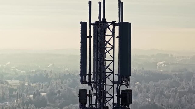 Frosty telecom cell tower with antenna panels rising above a misty winter landscape at sunrise, soft haze and copy space for technology or connectivity concepts.