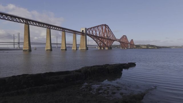 Aerial view of the magnificent red Forth Bridge over calm blue waters, a majestic feat of engineering, South Queensferry, Scotland, United Kingdom.