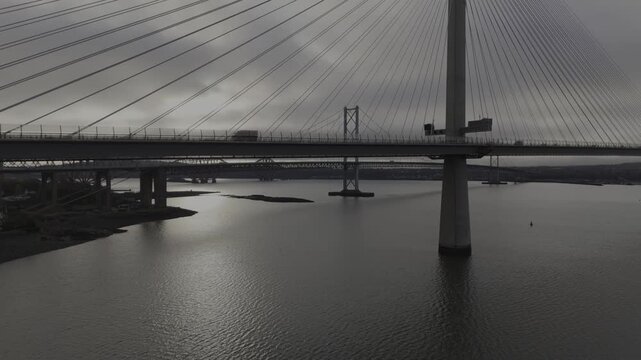 Aerial view of the Queensferry Crossing bridge over the calm, reflective waters under a cloudy sky, South Queensferry, United Kingdom.