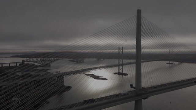 Aerial view of three bridges spanning the Firth of Forth, their structures contrasting against the moody, overcast sky, South Queensferry, United Kingdom.