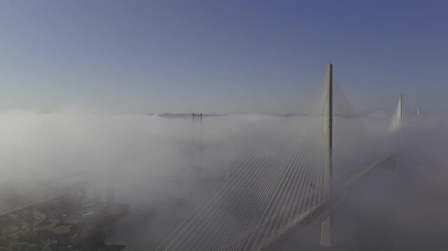 Aerial view of the towering Queensferry Crossing bridge piercing through a sea of dense fog, creating a surreal and ethereal landscape, South Queensferry, United Kingdom.