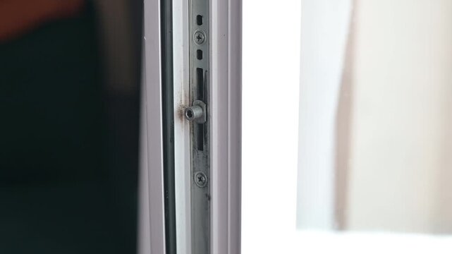 A person uses a power drill to install screws into a window frame, focusing on home improvement and maintenance.