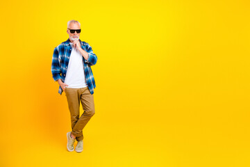Stylish senior man in sunglasses posing casually against bright yellow background wearing plaid...