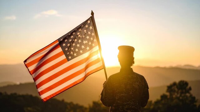 Silhouette of a soldier holding an American flag against a sunset background in the mountains during golden hour