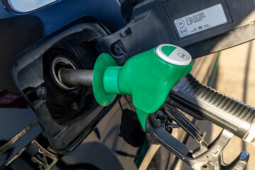 Obraz premium Green fuel dispenser inserted into the fuel filler of a car, filling up a car, rising fuel prices in the world