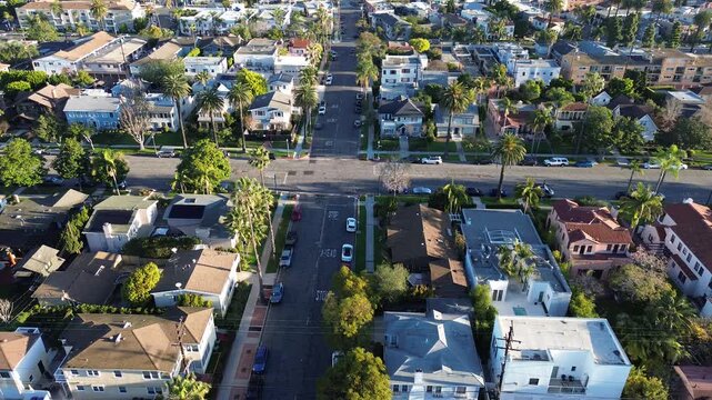Homes near Coronado Ave and E Ocean Blvd form tight Bluff Park grid with visible STOP markings and parked cars along tree lined streets. Palm shadows, textured lawns, warm light, Long Beach, CA