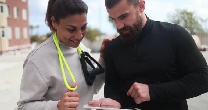 Mature latin woman and her personal trainer checking workout plan on tablet outdoor - Sport, healthy lifestyle and fitness concept