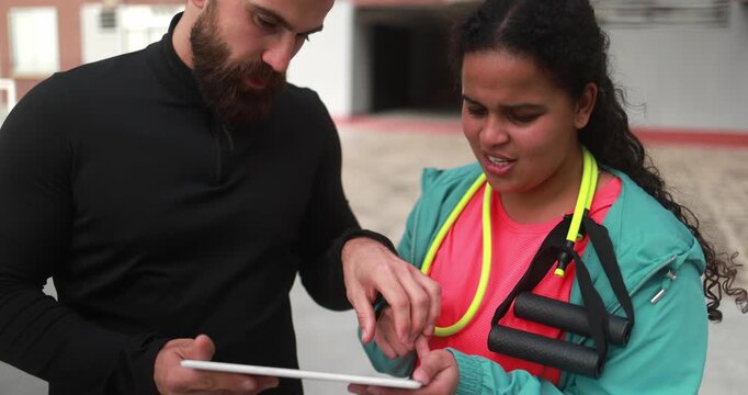 Personal trainer explaining workout plan to curvy african american girl on tablet - People, sport and diet concept