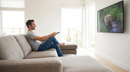 Obraz premium Man sitting cross-legged on sofa watching TV