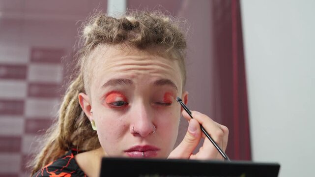 Young woman with dreadlocks applying red eyeshadow
