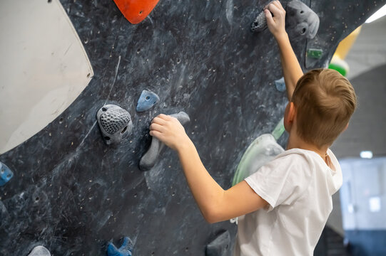 Side View of a Young Boy Climbing an Indoor Bouldering Wall with Colorful Holds at a Sporting Gym