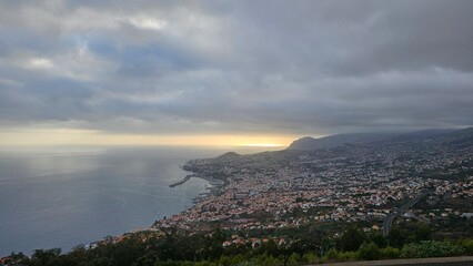 Dramatic sunset over Funchal, Madeira island with golden light breaking through storm clouds above the Atlantic Ocean and the sprawling coastal city below. © Sebastiaan89