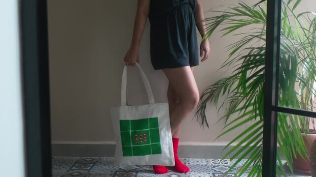 Woman presenting a custom eco-friendly tote bag with green and red design, showing modern fashion and conscious lifestyle choices for urban living