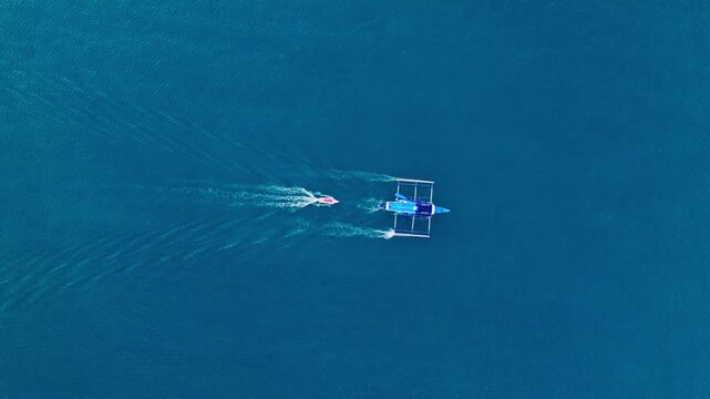 Drone ascends showing large outrigger towing small pink boat across open water