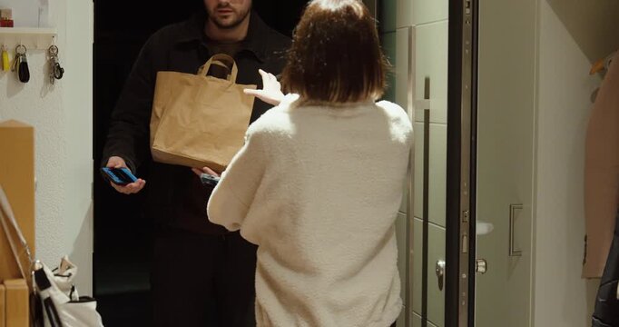Woman receiving a grocery delivery at the door and completing contactless payment using her smartphone, illustrating digital payment, ecommerce, and modern consumer lifestyle.