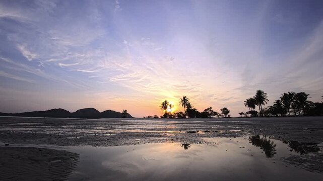 Tropical sunset behind palm trees with reflections on wet tidal sand