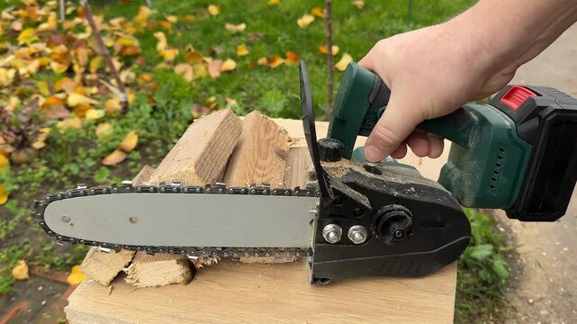 Closeup of hands using cordless chainsaw on split firewood outdoors, practical yard work and home improvement, autumn leaves suggest fall cleanup before Thanksgiving
