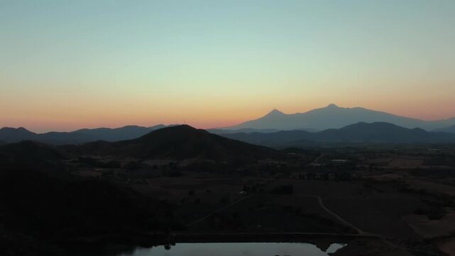 Backward drone view of Presa de Huizilacates with Volc&aacute;n de Colima and Nevado de Colima in the background at dawn in Jalisco.