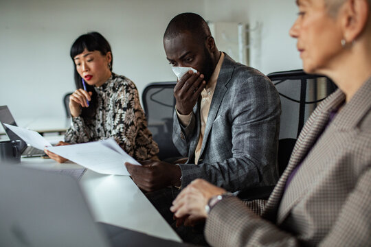 Business team reviewing documents as colleague covers nose with tissue in office