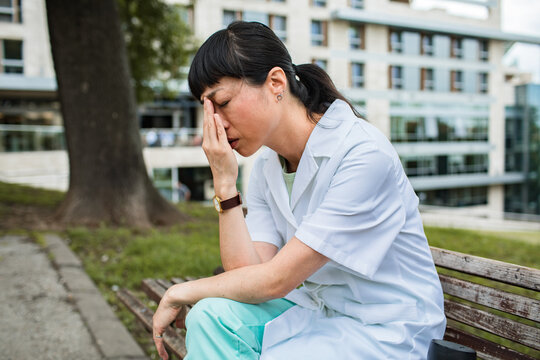 Stressed healthcare worker resting on bench outside hospital