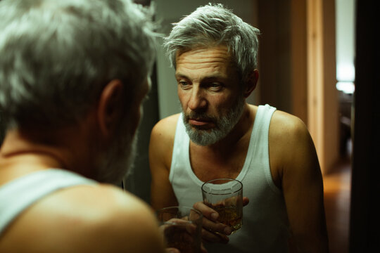 Middle-aged man with whiskey glass at bathroom mirror