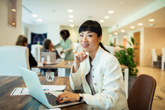 Smiling businesswoman working on laptop in modern office