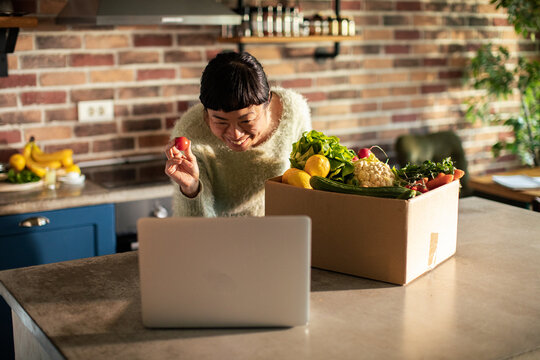 Woman on video call with produce delivery box in home kitchen